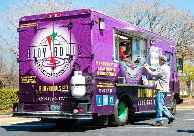 Buoy Bowls employee in food truck serving açaí bowl to customer