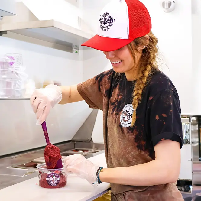 A smiling Buoy Bowls employee making an açaí bowl