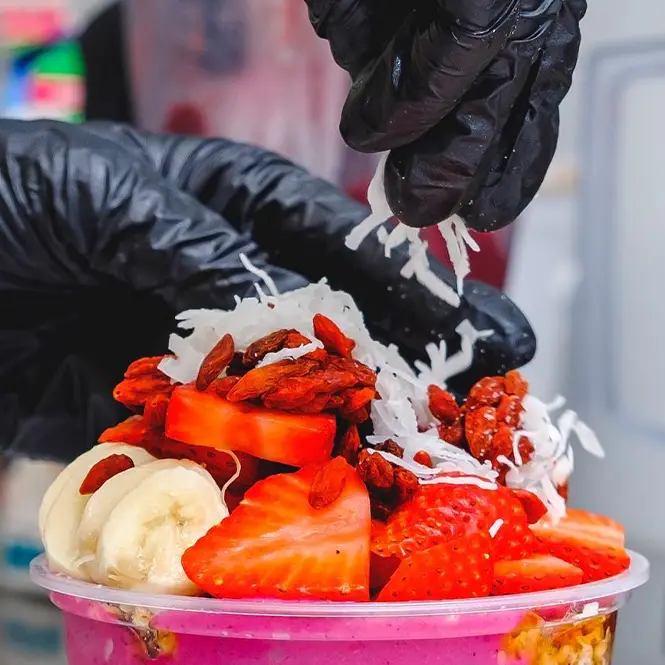 A Buoy Bowls employee putting coconut and goji berries on an açaí bowl