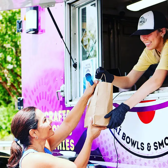 A Buoy Bowls employee smiling and handing a bag of product to a customer