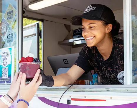A Buoy Bowls employee smiling and handing an açaí bowl out of the purple truck window