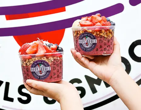 A Buoy Bowls employee holding two Buoy Bowls açaí bowls in front of the truck