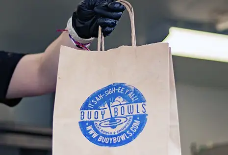 Buoy Bowls employee holding brown bag of products