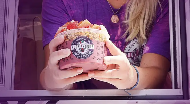 Buoy Bowls employee in food truck window holding açaí bowl
